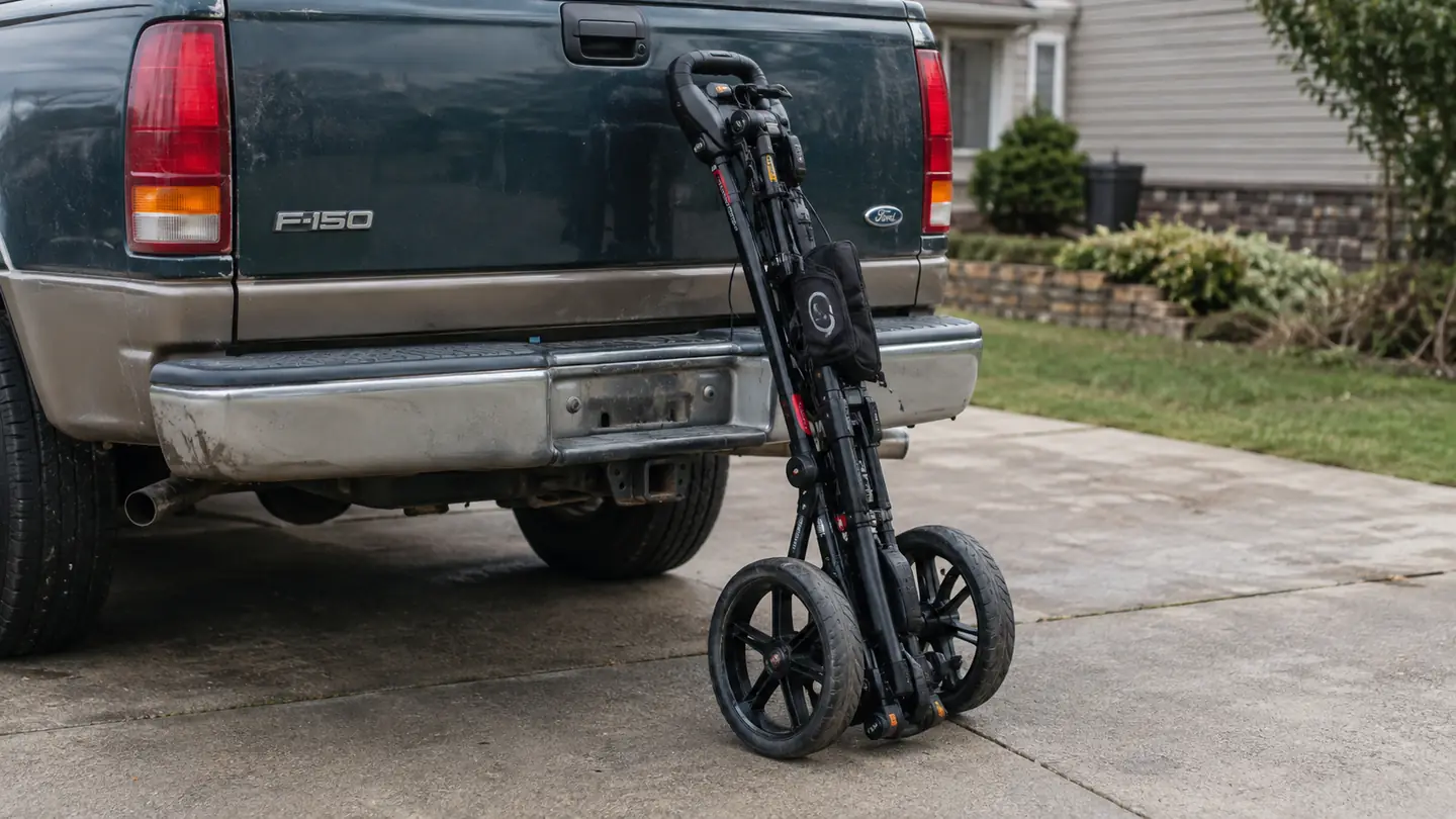 A folded golf push cart leaning against the tailgate of an older pickup truck in a driveway