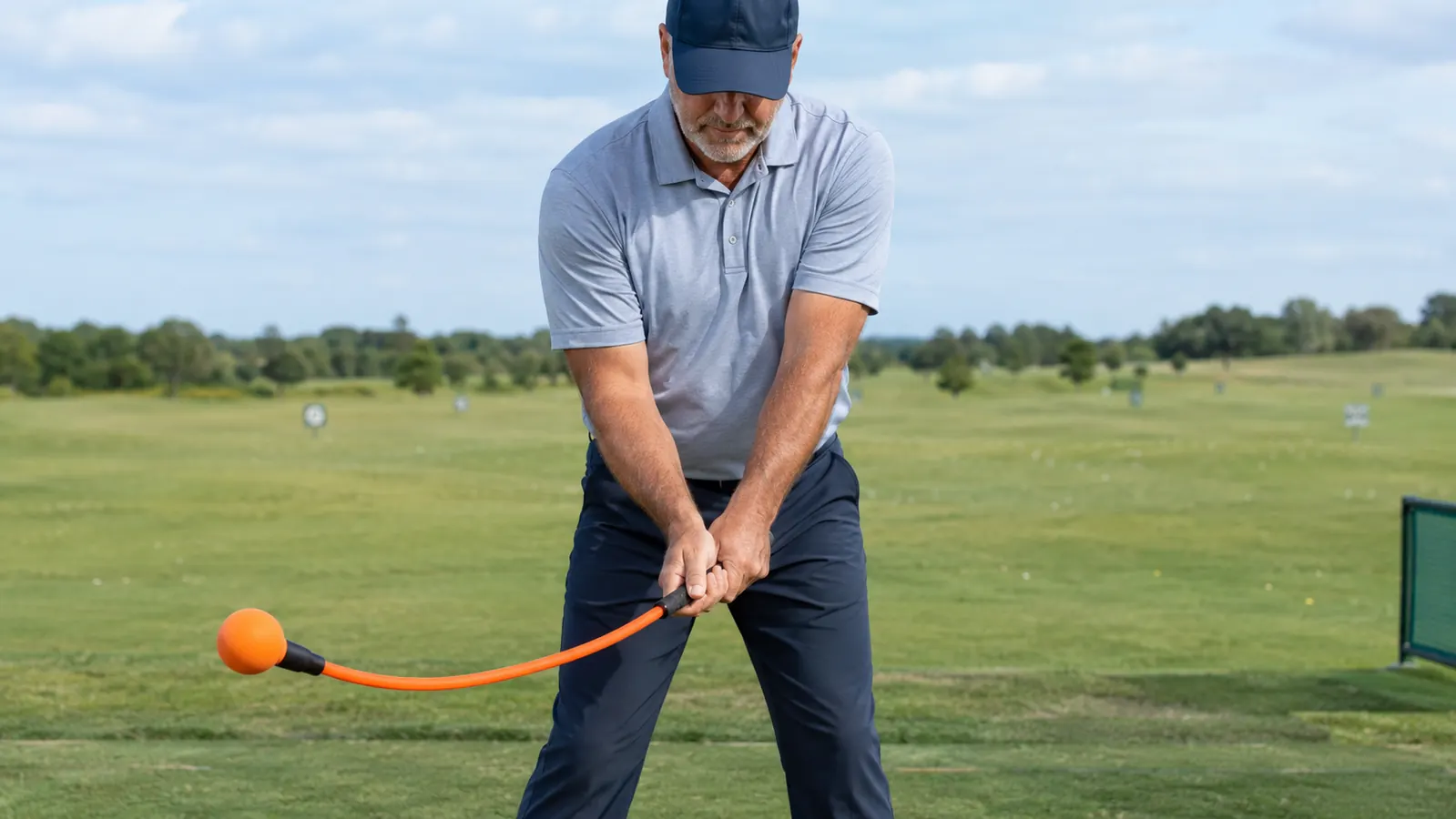 A golfer holding a weighted swing trainer on a practice range
