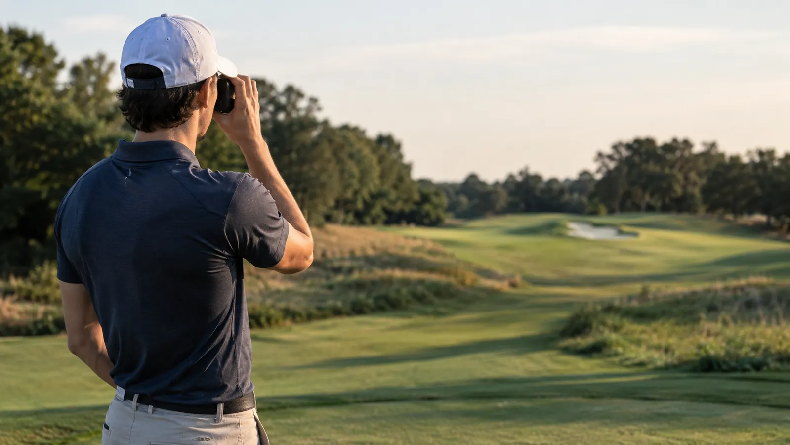 A golfer on a tee box looking through a rangefinder at a fairway bunker