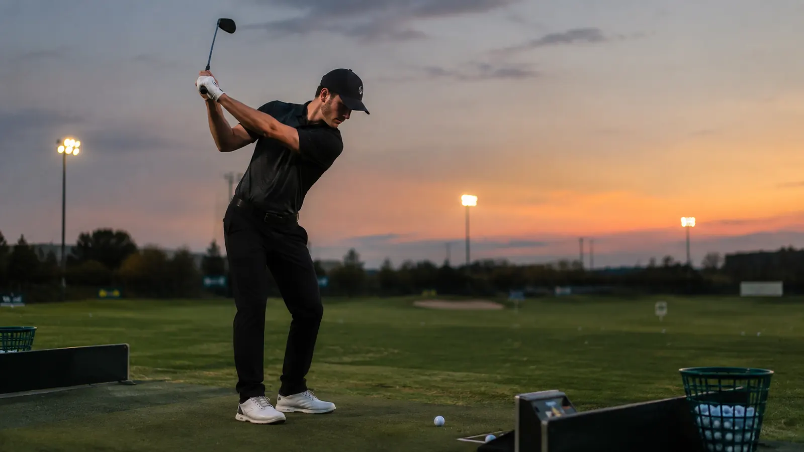 A golfer practicing a smooth tempo swing on a driving range at dusk